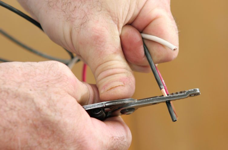 An electrician's hands using wire strippers to remove the insulation from copper wire.